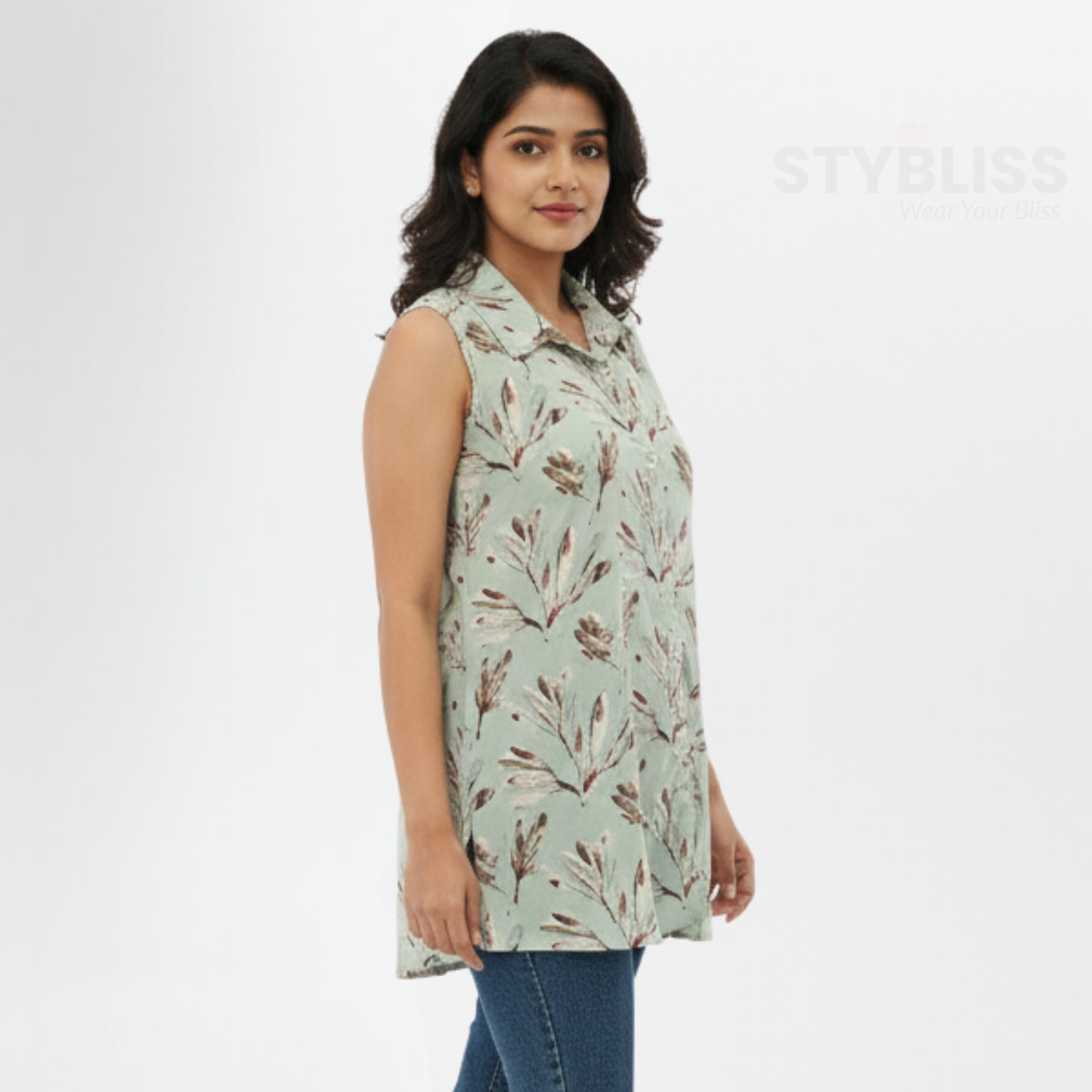 Woman wearing a light green sleeveless shirt with a leaf pattern on a white background, branded 'STYBLISS'.